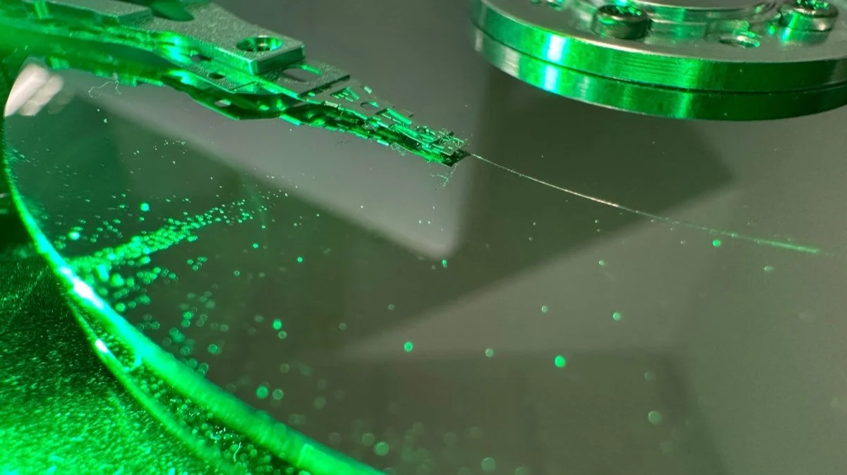 Close-up of an open hard drive showing the platter and read/write head assembly under green lab lighting during professional hard drive data recovery.