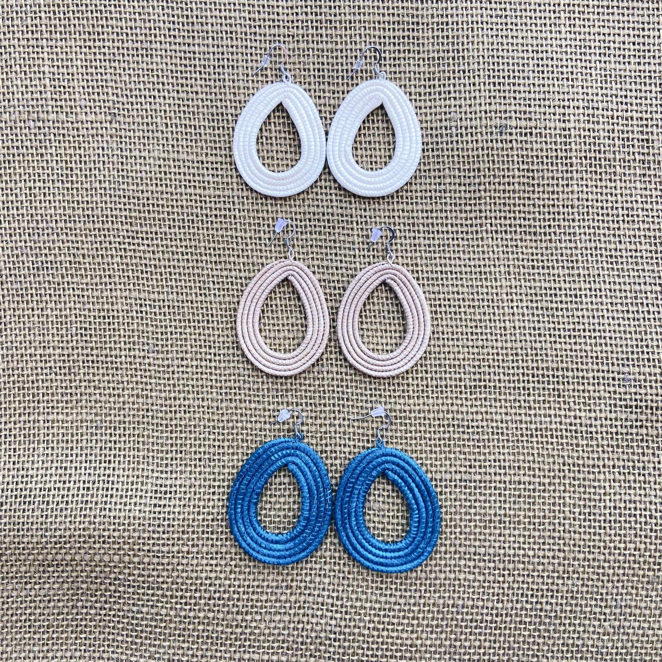 Three pairs of hand woven sisal loop earrings in white, tea, and celestial blue on a burlap background.