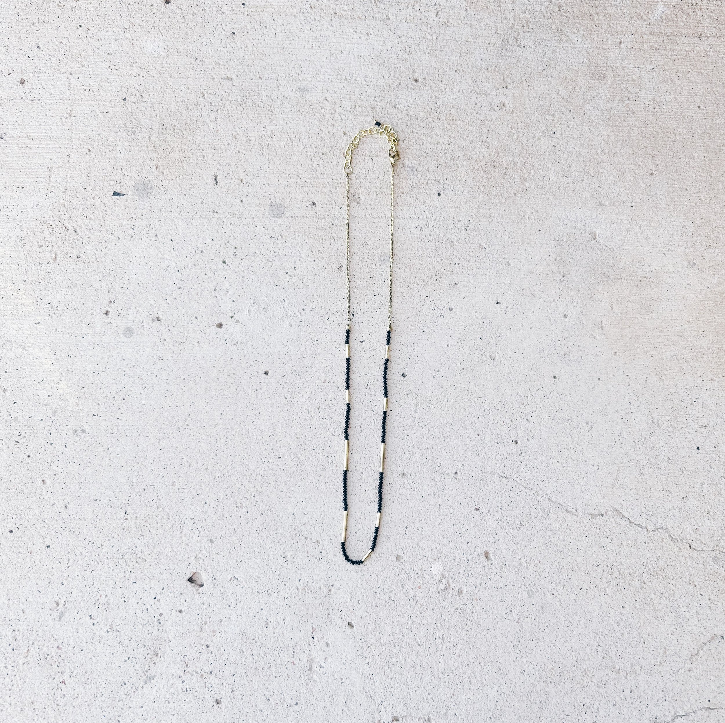 From a distance, the Morse Code Necklace has black seed beads and brass tube beads at the bottom and brass chain with an extender at the top.