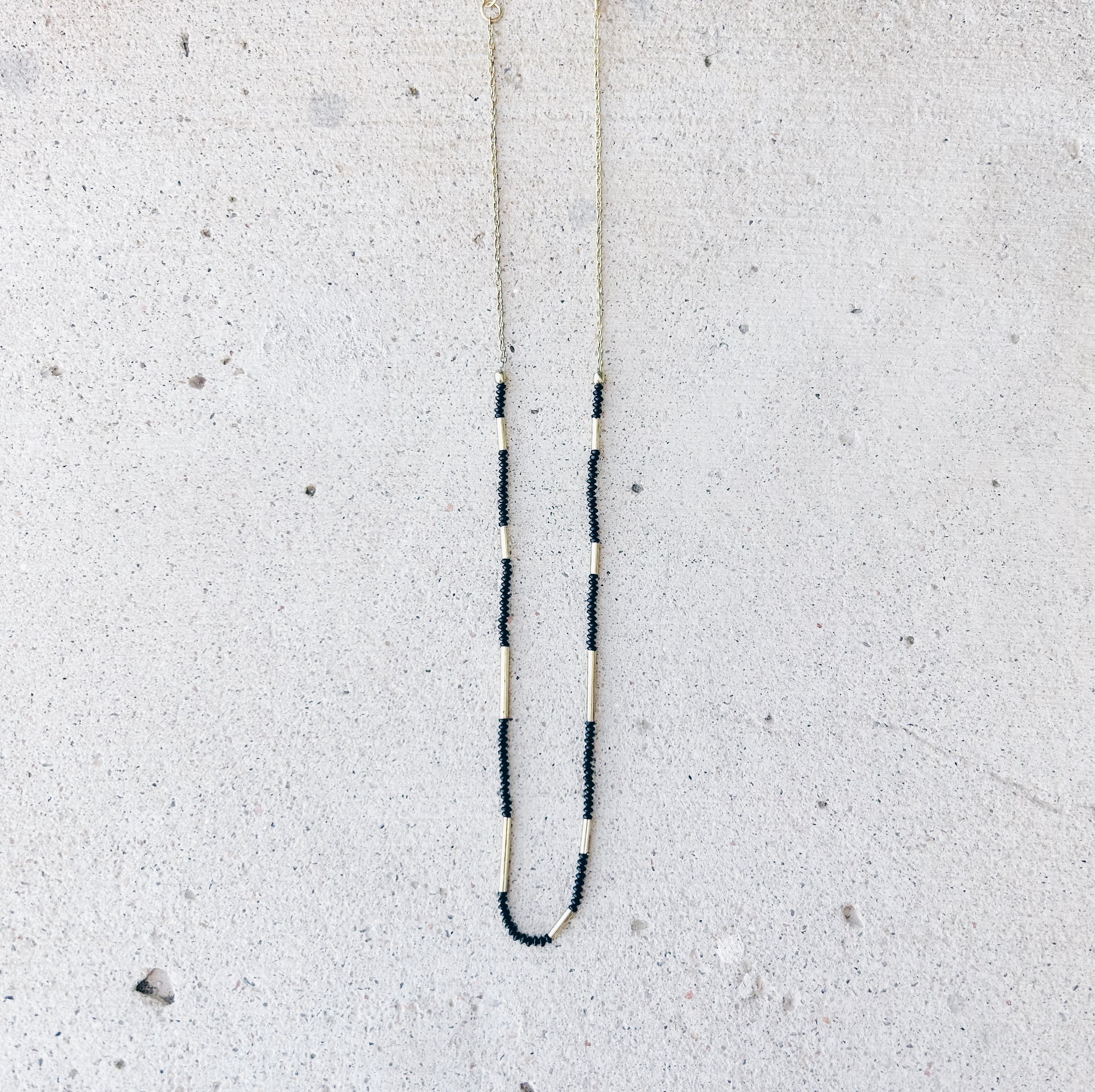 The Morse Code Necklace features tiny black seed beads and brass tube beads in an intricate pattern.
