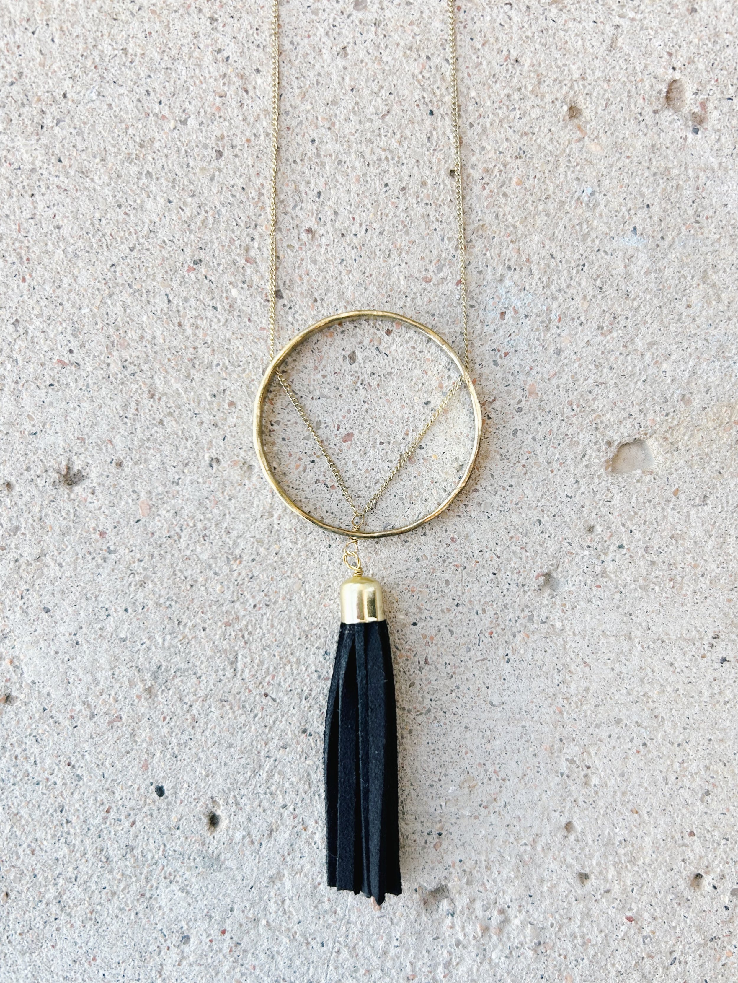 The skinny chain of the Ellaria Tassel Necklaces passes through the circle charm to form a triangle.
