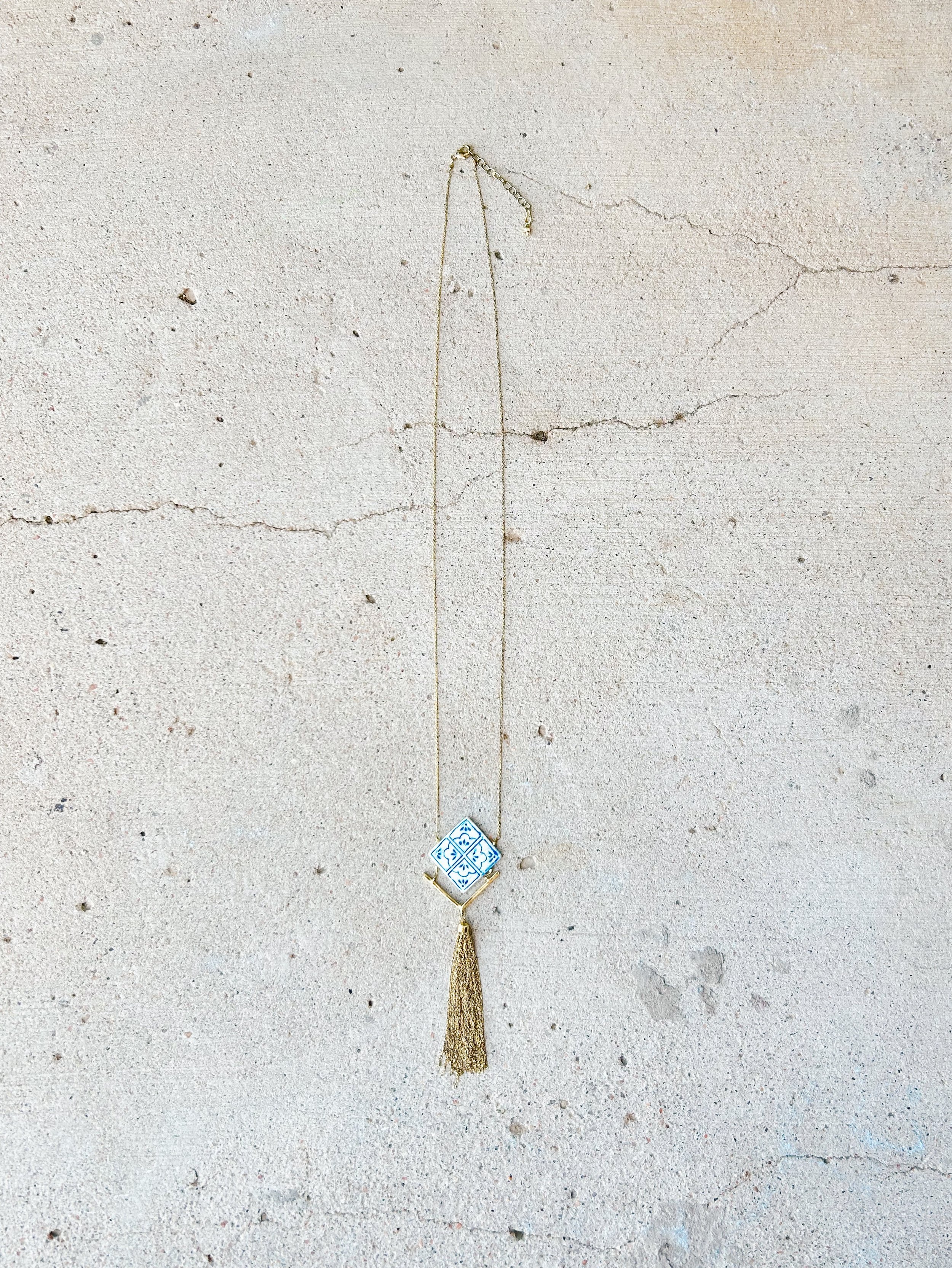The Mallorca Tile Necklace has a skinny brass chain and features a hand-painted bone tile with chain tassel detail.