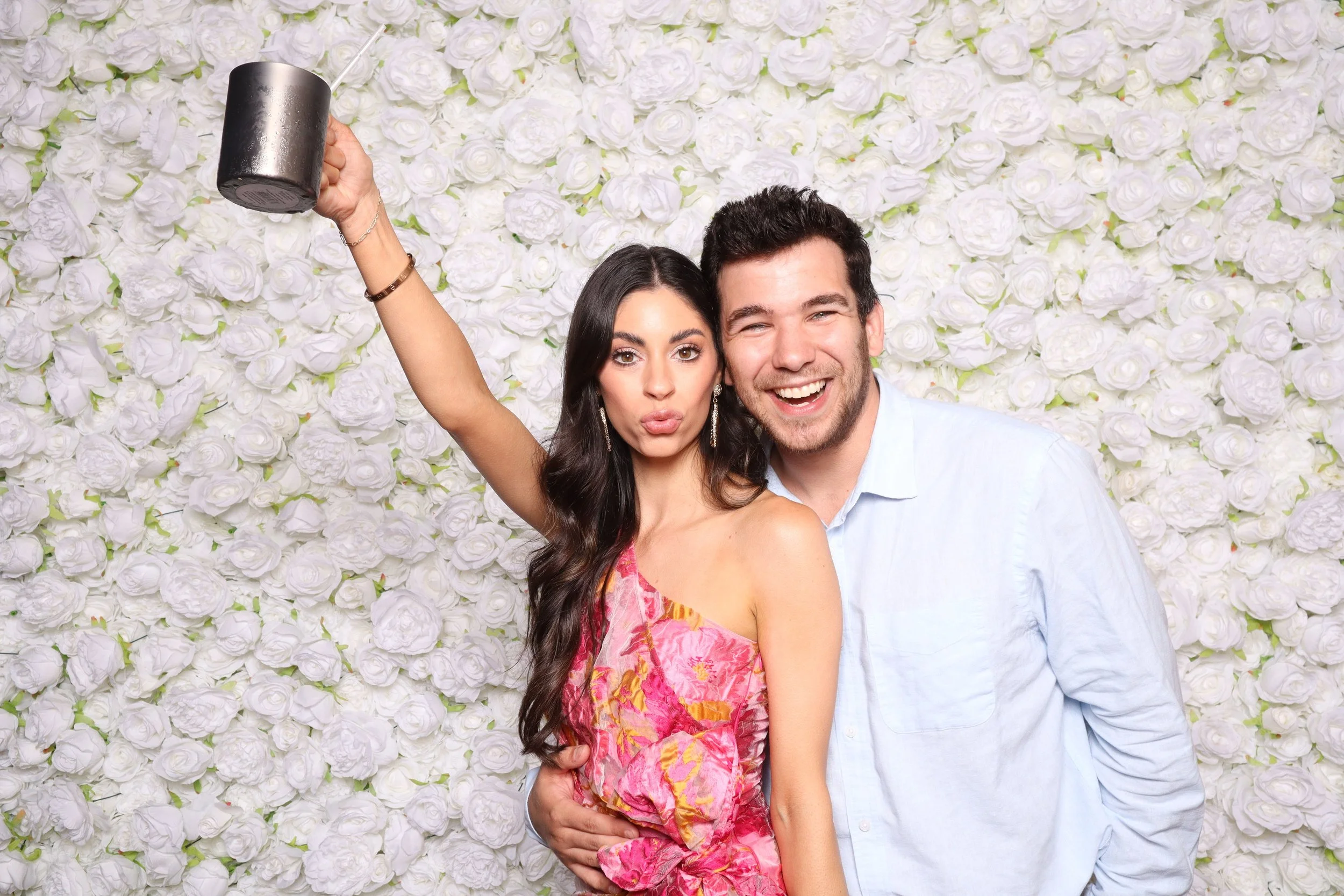 A couple taking a photo booth pic with our white rose backdrop.