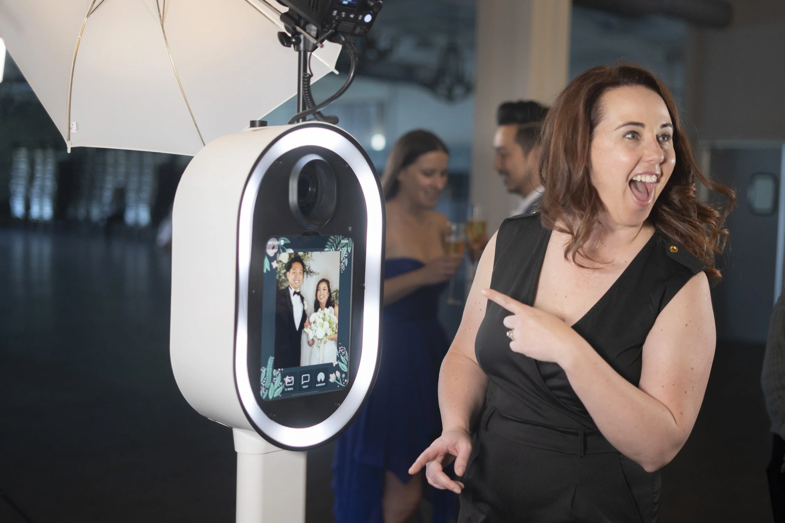 Woman smiling and pointing at a photo booth during a wedding reception