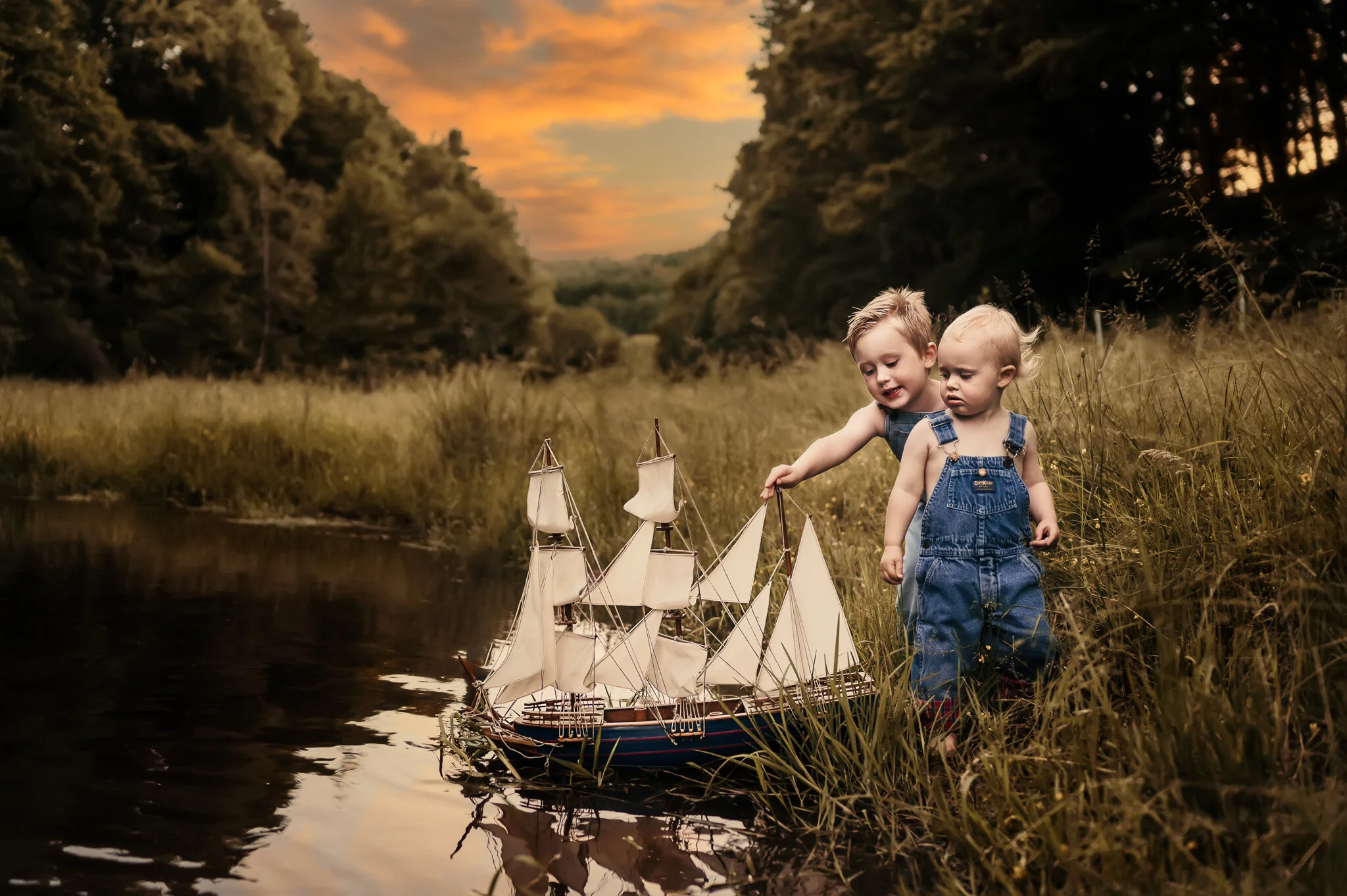 Two young boys playing with grandfather's ship in water at sunset