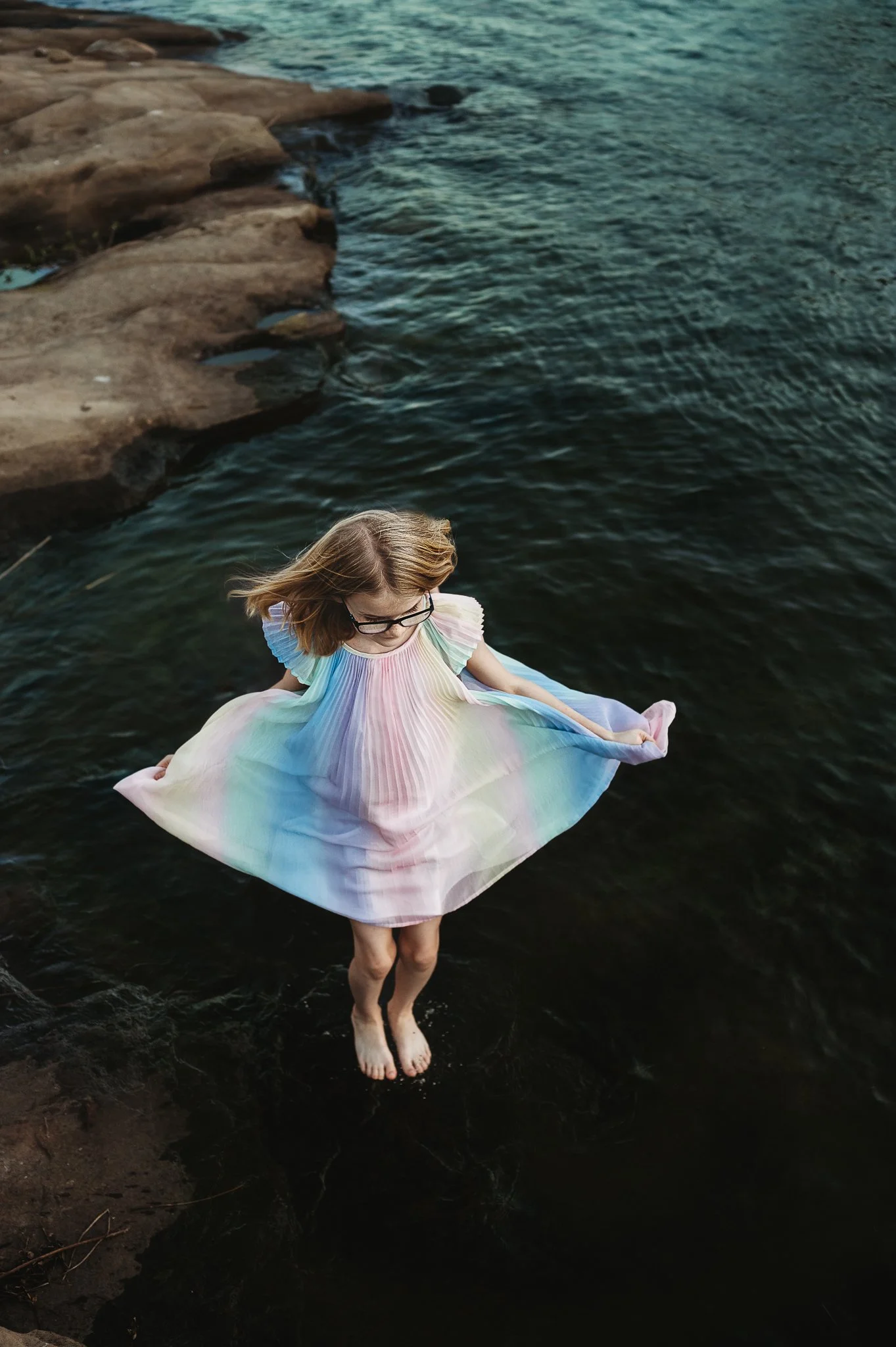 Little girl wearing pastel rainbow dress jumping in shallow water