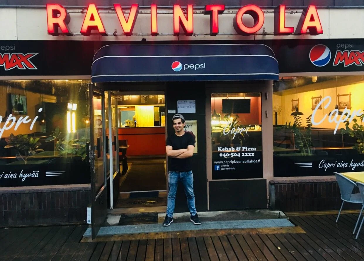 Azad seisoo ravintolansa edustalla ja hymyilee ystävällisesti.