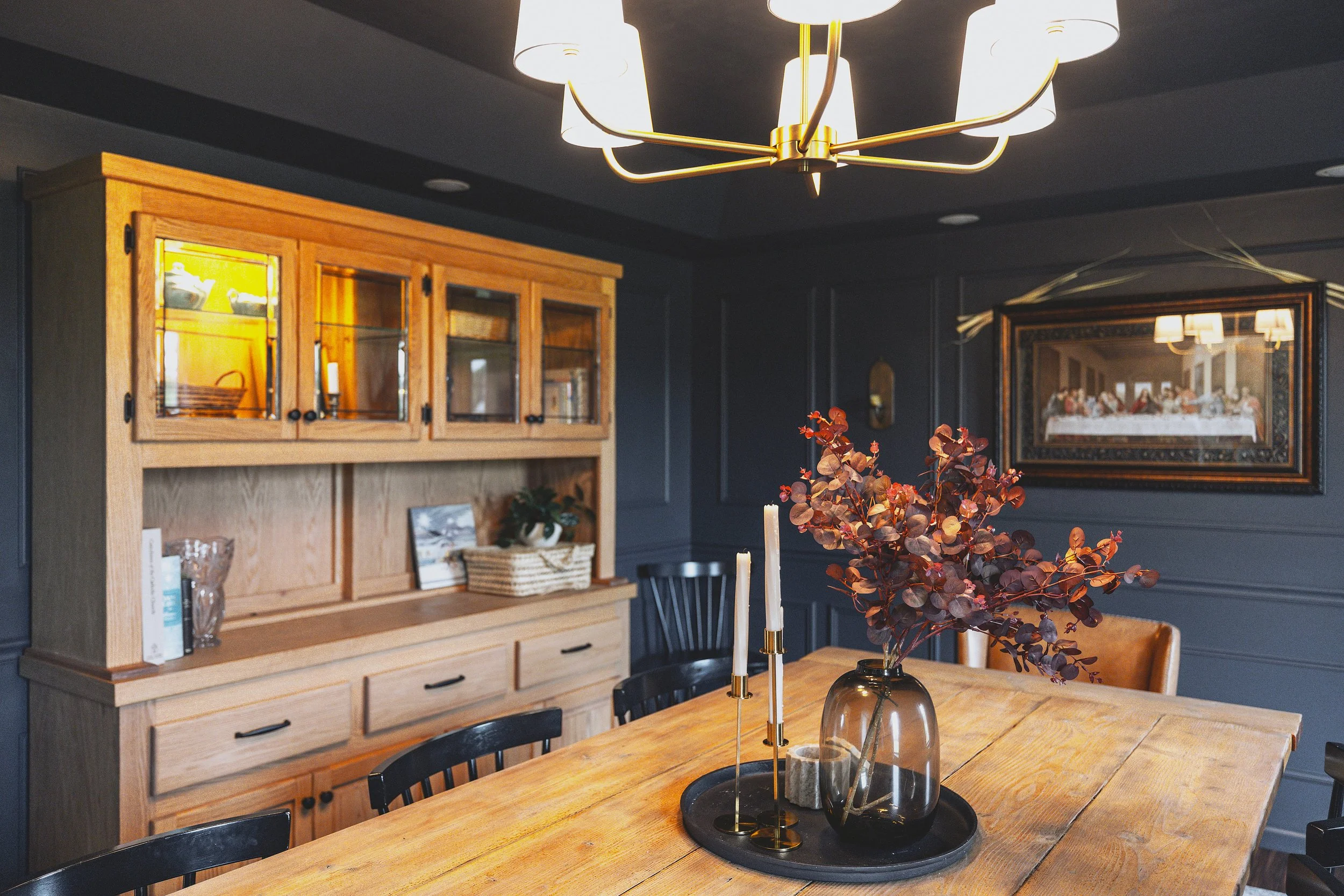 Brass chandelier over dining table with wood hutch in background