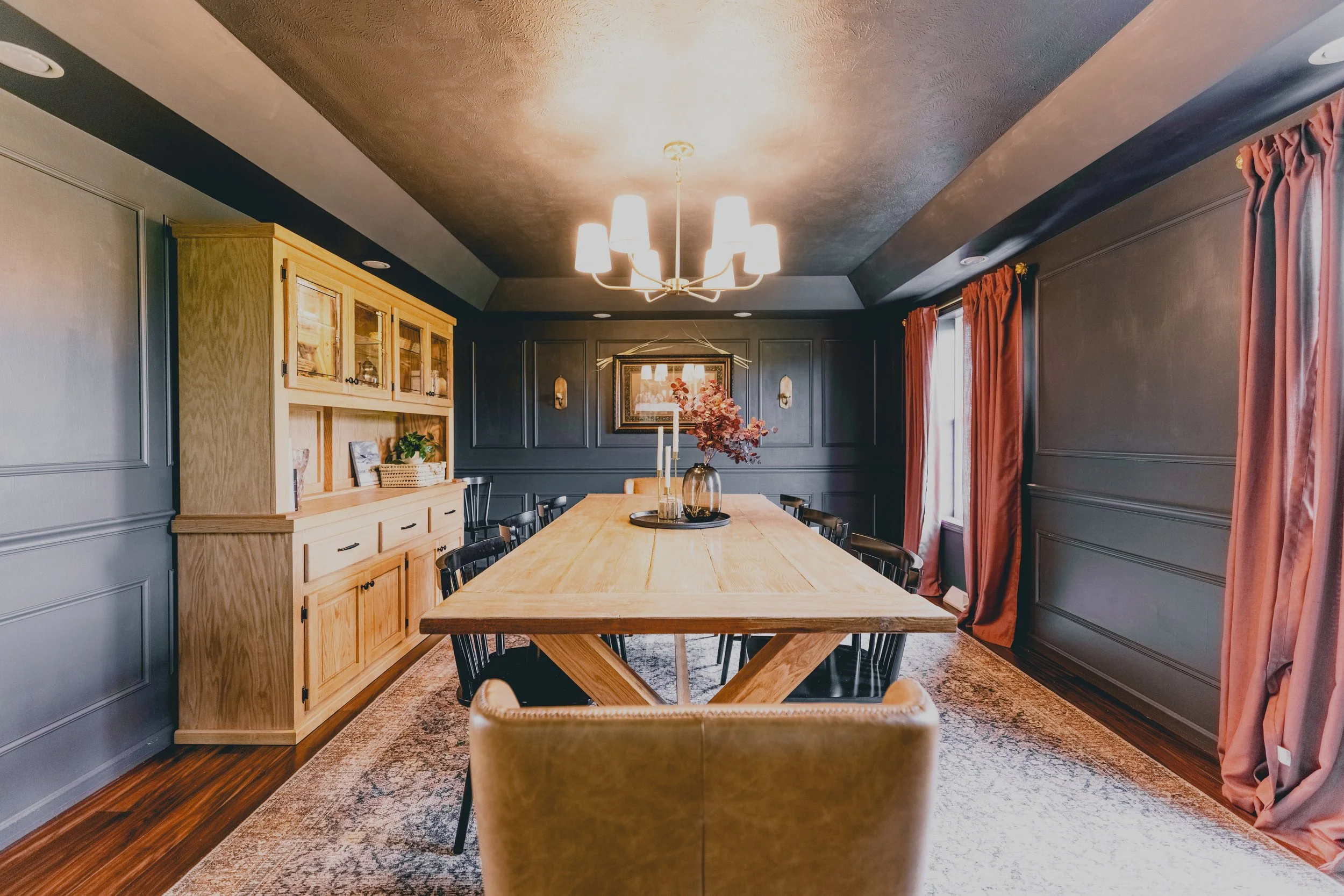 Full view of dining room table, black Windsor chairs, and burgundy linen curtains