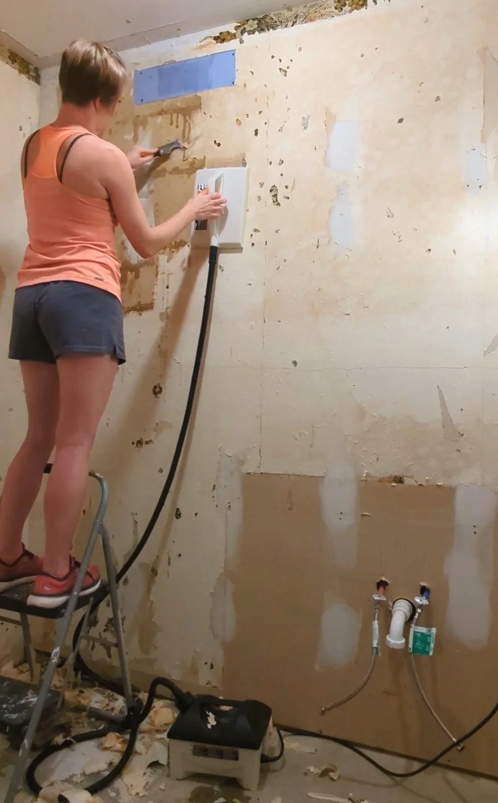 Woman in orange stripping wallpaper with steamer