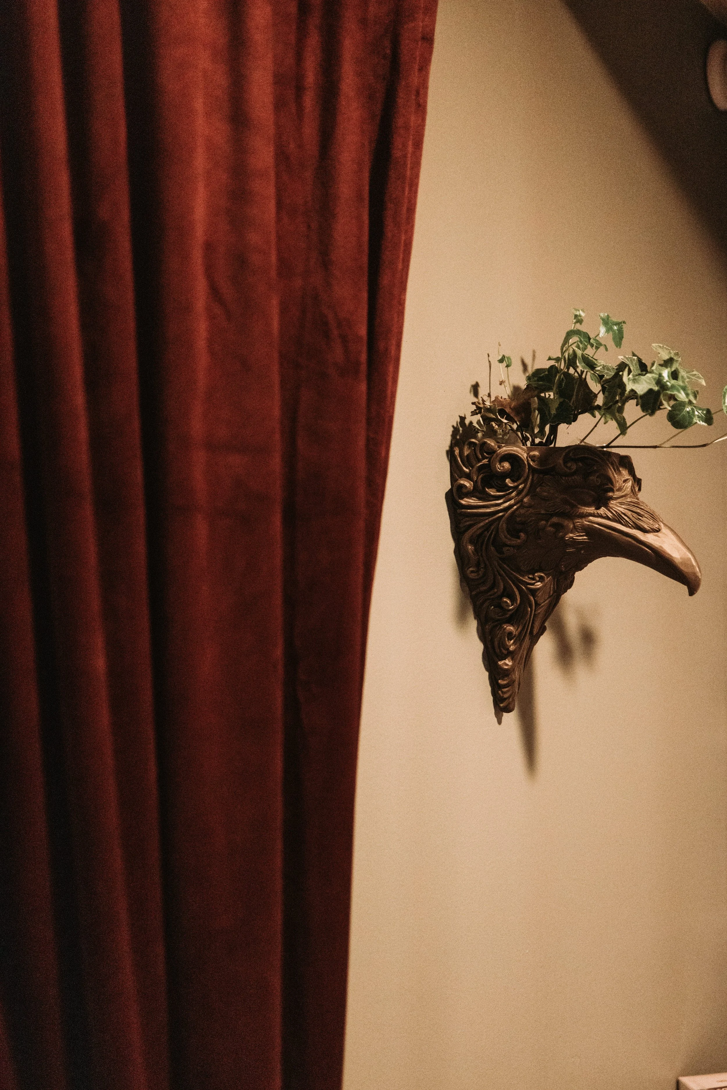 Carved raven wall sconce planter beside deep red velvet curtain