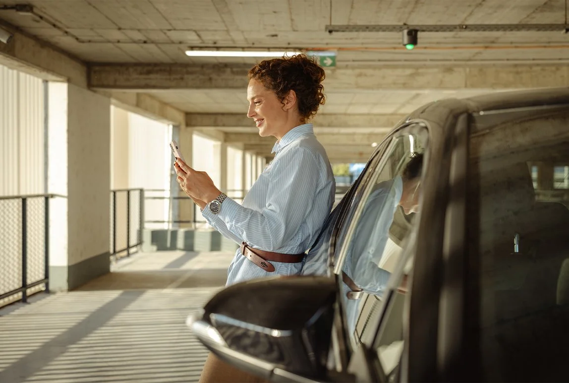 Woman on her phone leaning against a car in a parking lot.