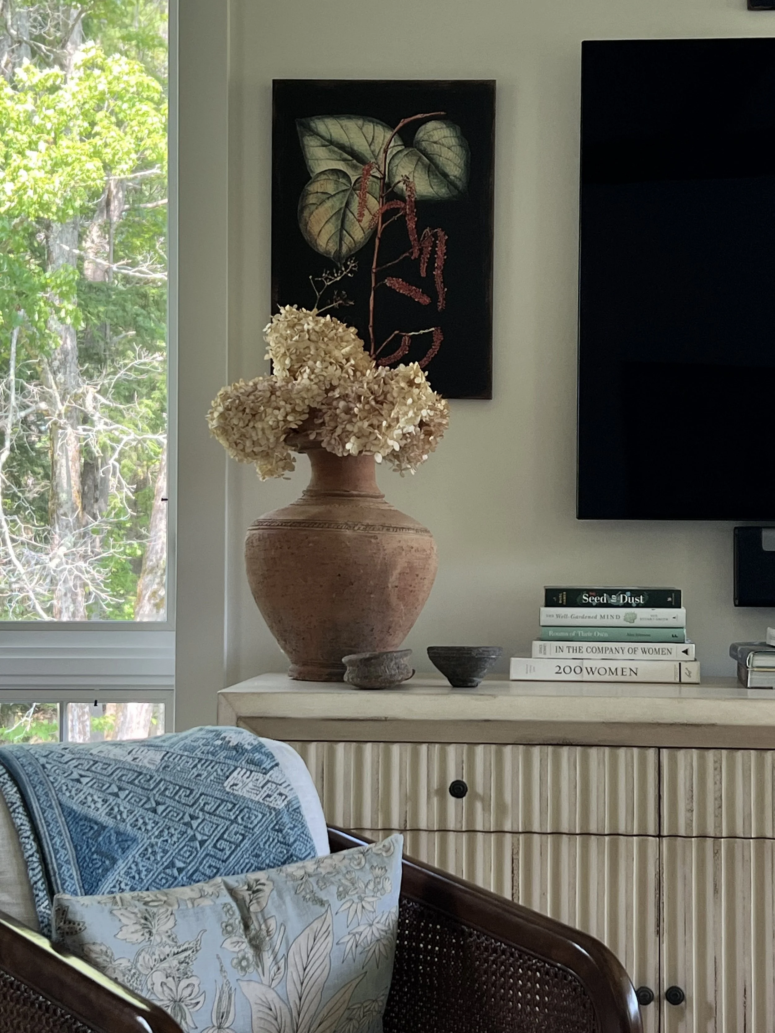 Dried hydrangeas in a clay vase beside a stack of books