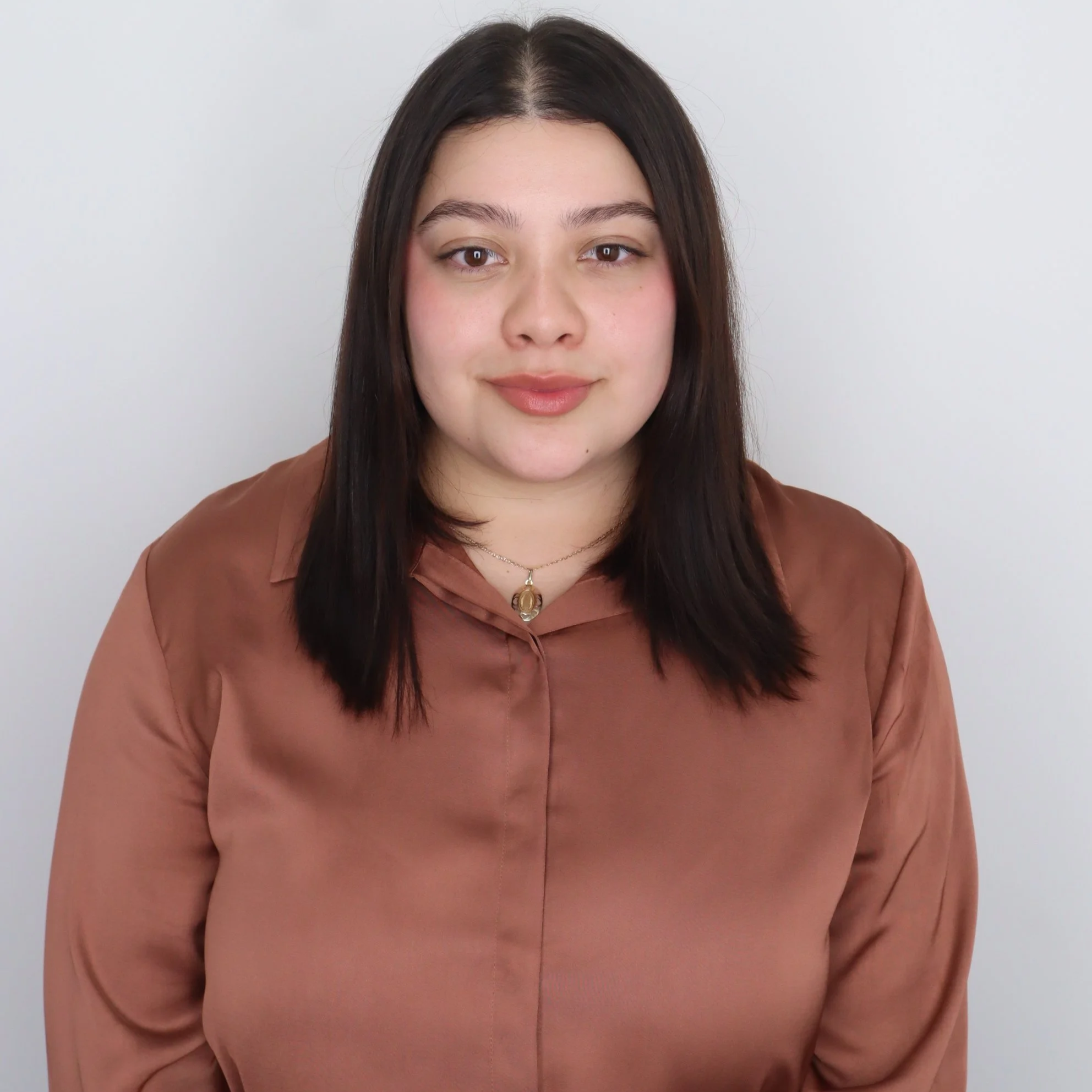 Jennifer, a Hispanic female, smiles softly at the camera. She has shoulder length dark brown hair and is wearing a brown shirt.