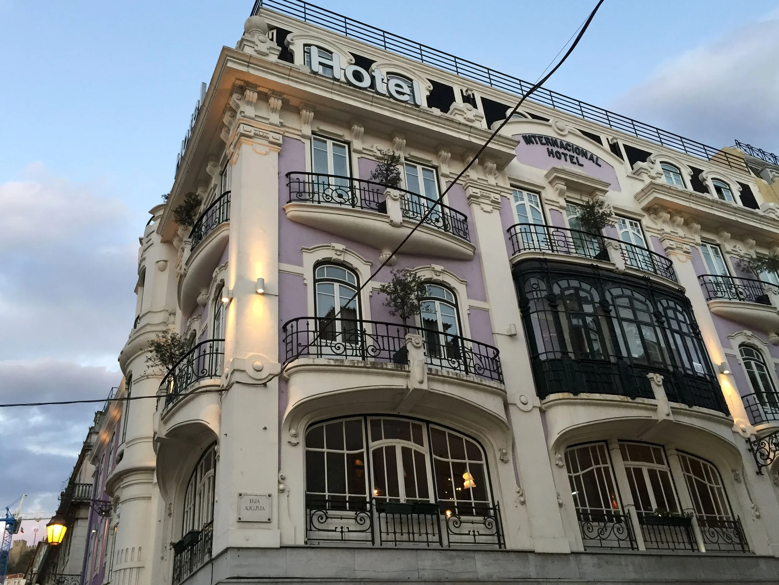 International Design Hotel in Lisbon, Portugal, with ornate narrow balconies and a purple and cream coloured facade. Blue sky and the Castelo de São Jorge in the distance.