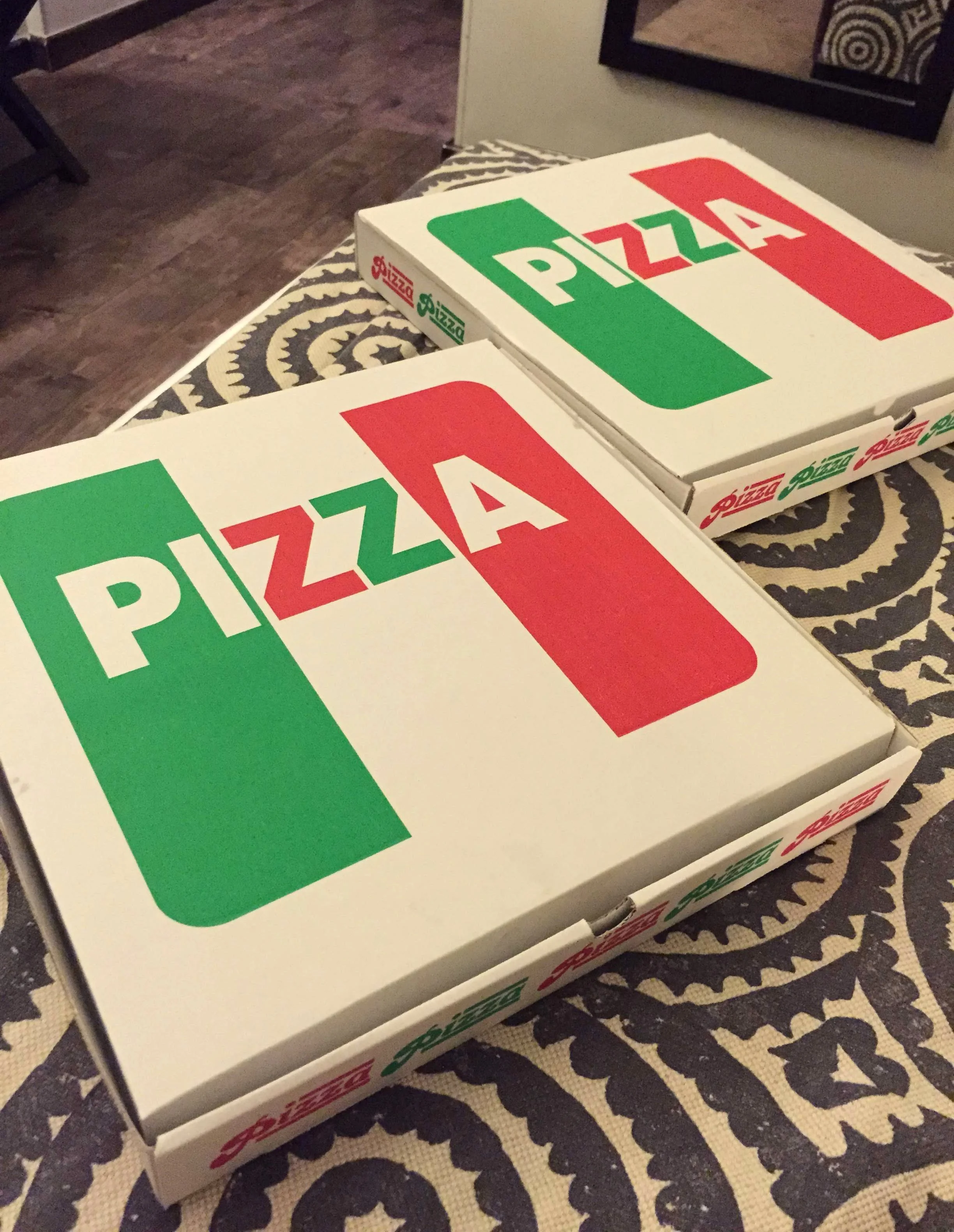 Two pazza boxes placed on top of hotel bed. The bedspread has a circular bold grey and cream pattern.