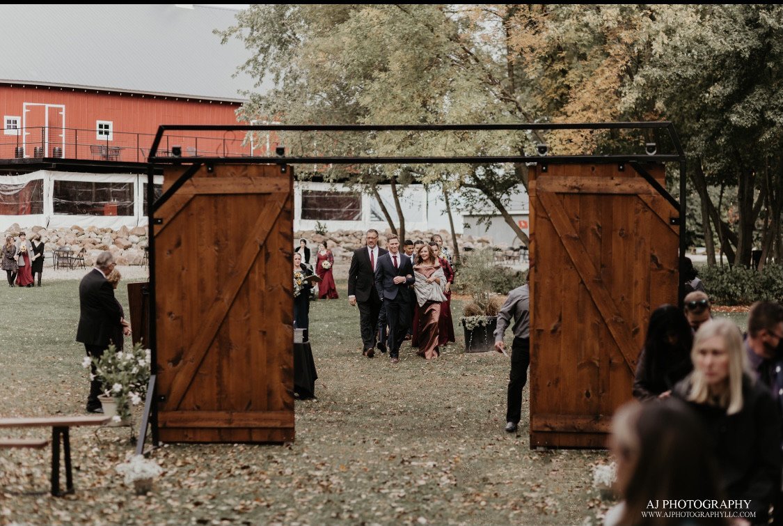 Wedding party walking through large barn doors toward an outdoor ceremony