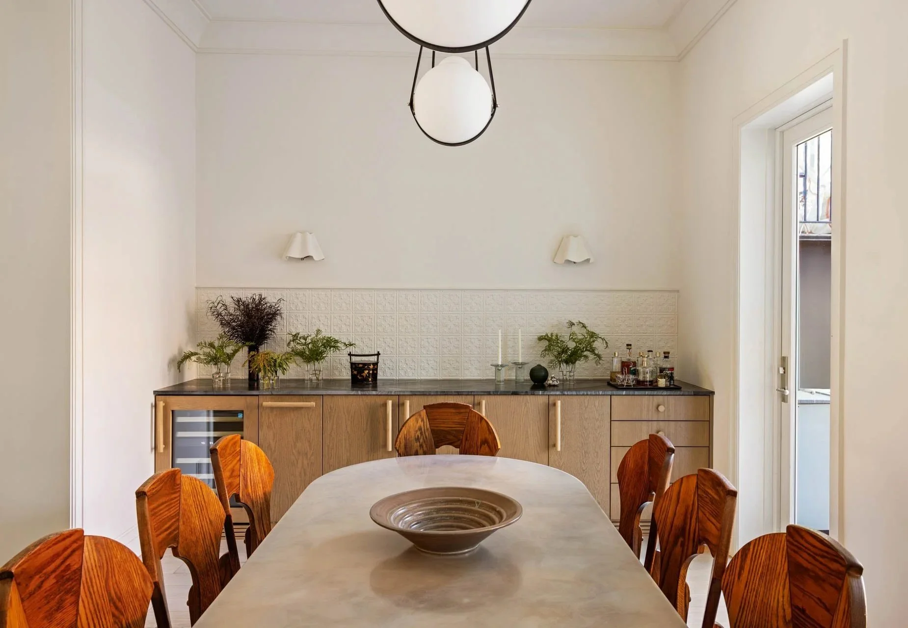 Dining room table with a dry bar and wine refrigerator built into custom cabinets against the far wall