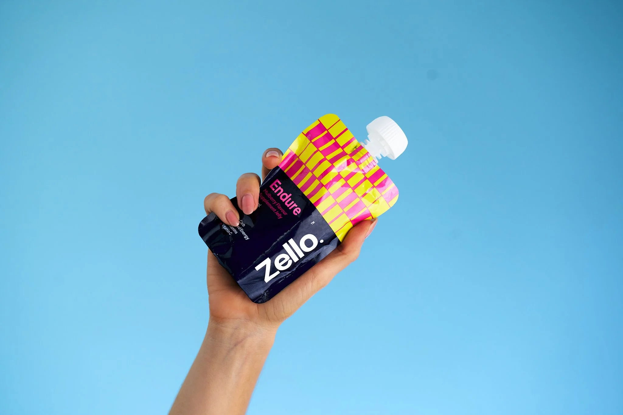A hand holding a colorful packet of Hello Zello Endure gel supplement against a blue background.