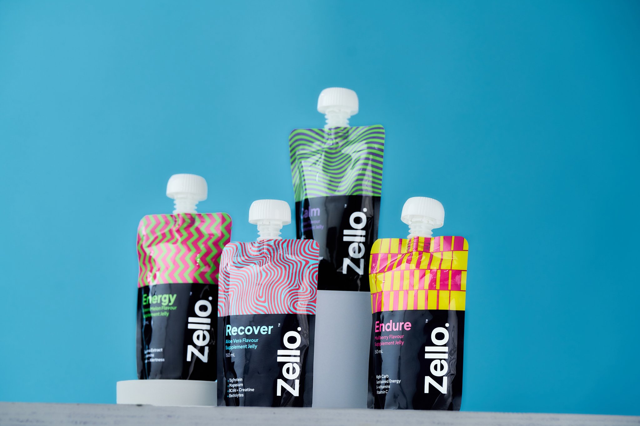 Four colorful Zellio supplement jelly pouches standing upright on a white surface against a blue background.