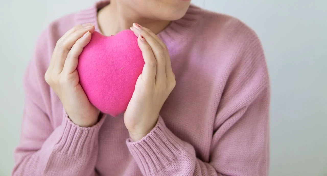 woman in a sweater hold a big stuffy heart