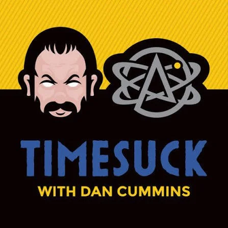 Logo for 'Timesuck with Dan Cummins' podcast featuring a cartoon man with dark hair and beard next to a stylized atom symbol.