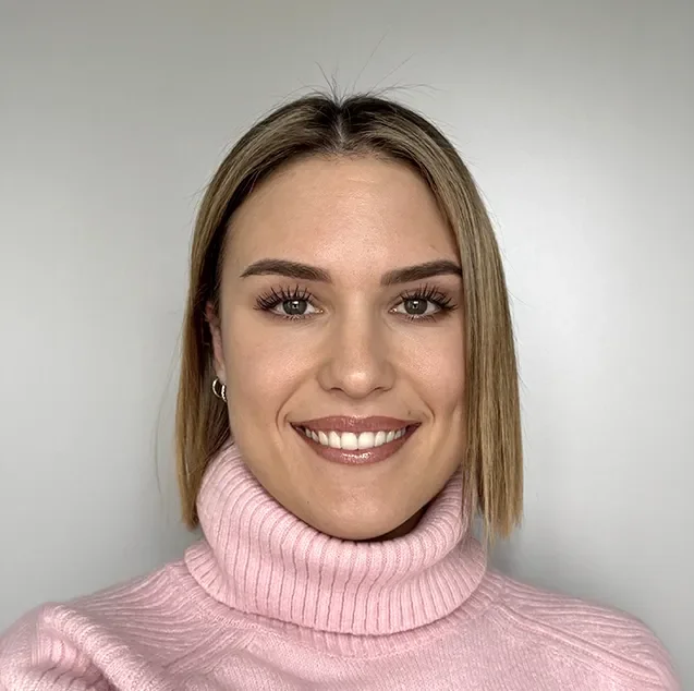 Nahaufnahme eines lachenden jungen Frau mit bunter Kleidung und blondem Haar vor einem weißen Hintergrund.