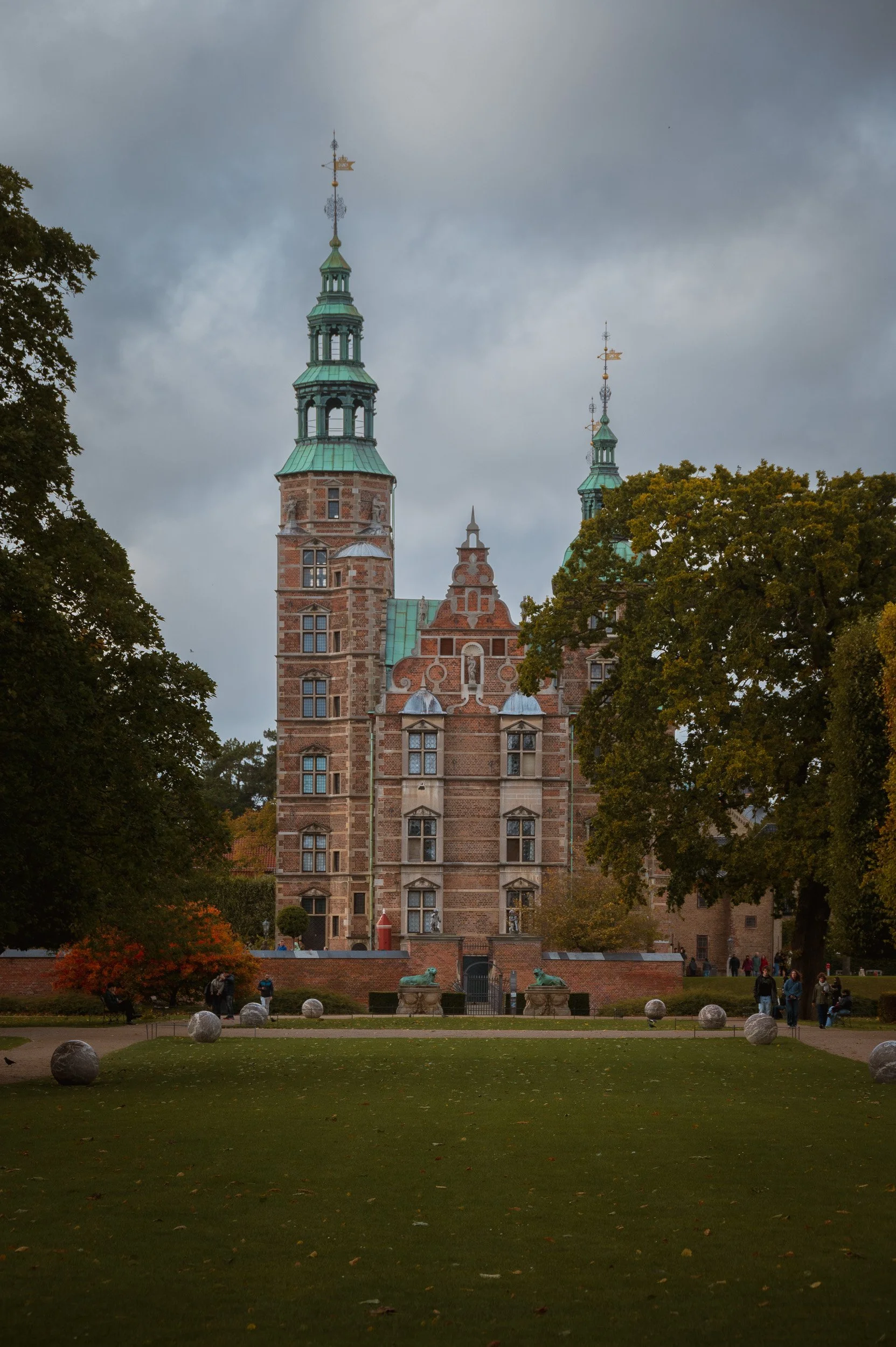 Landscape photography of Rosenborg Castle in Copenhagen, featuring its historic brick facade, green copper spires, and a moody sky.