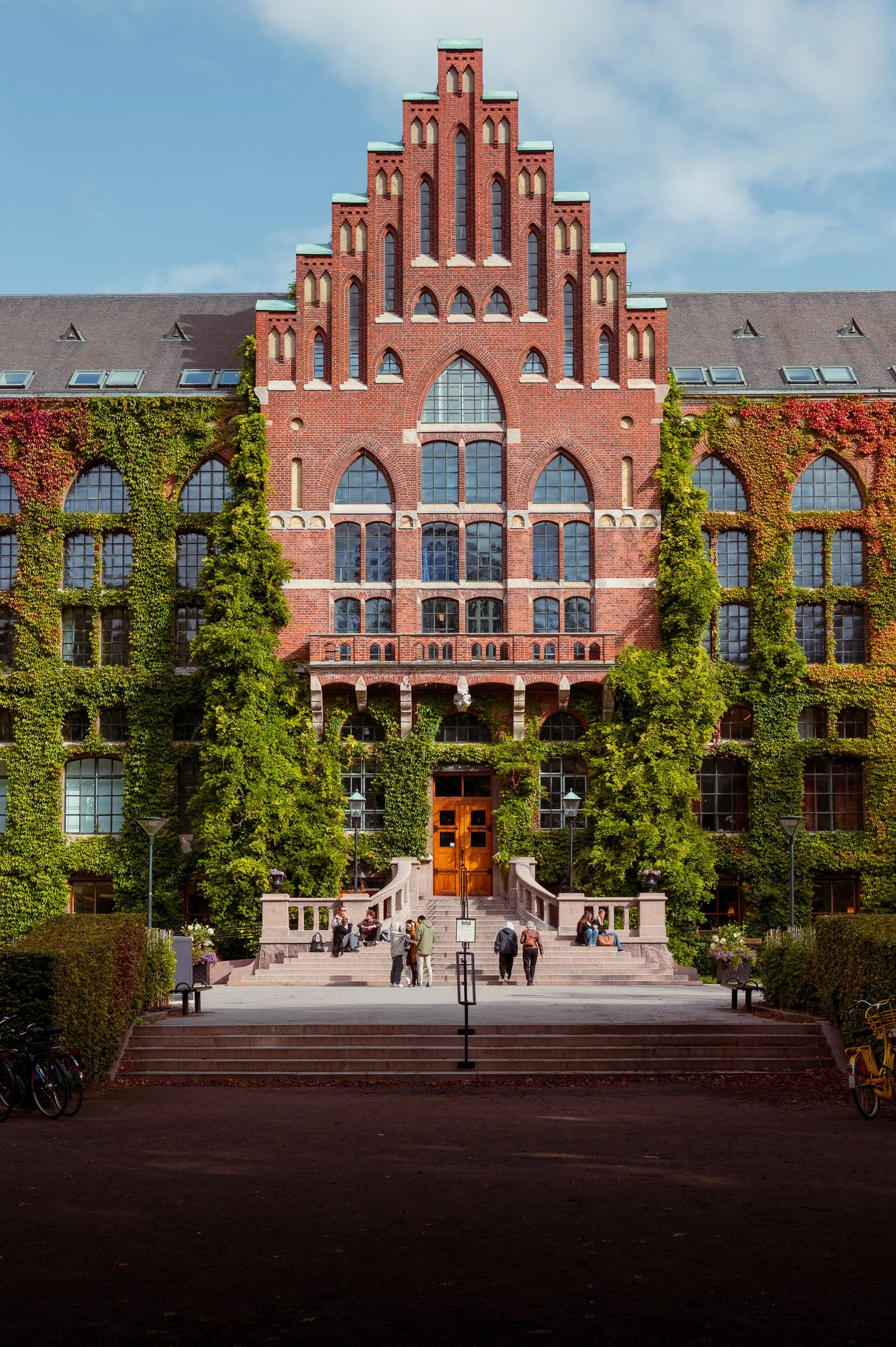 Architectural photography of the University Library in Lund, Sweden, featuring a historic red brick facade covered in lush green ivy.