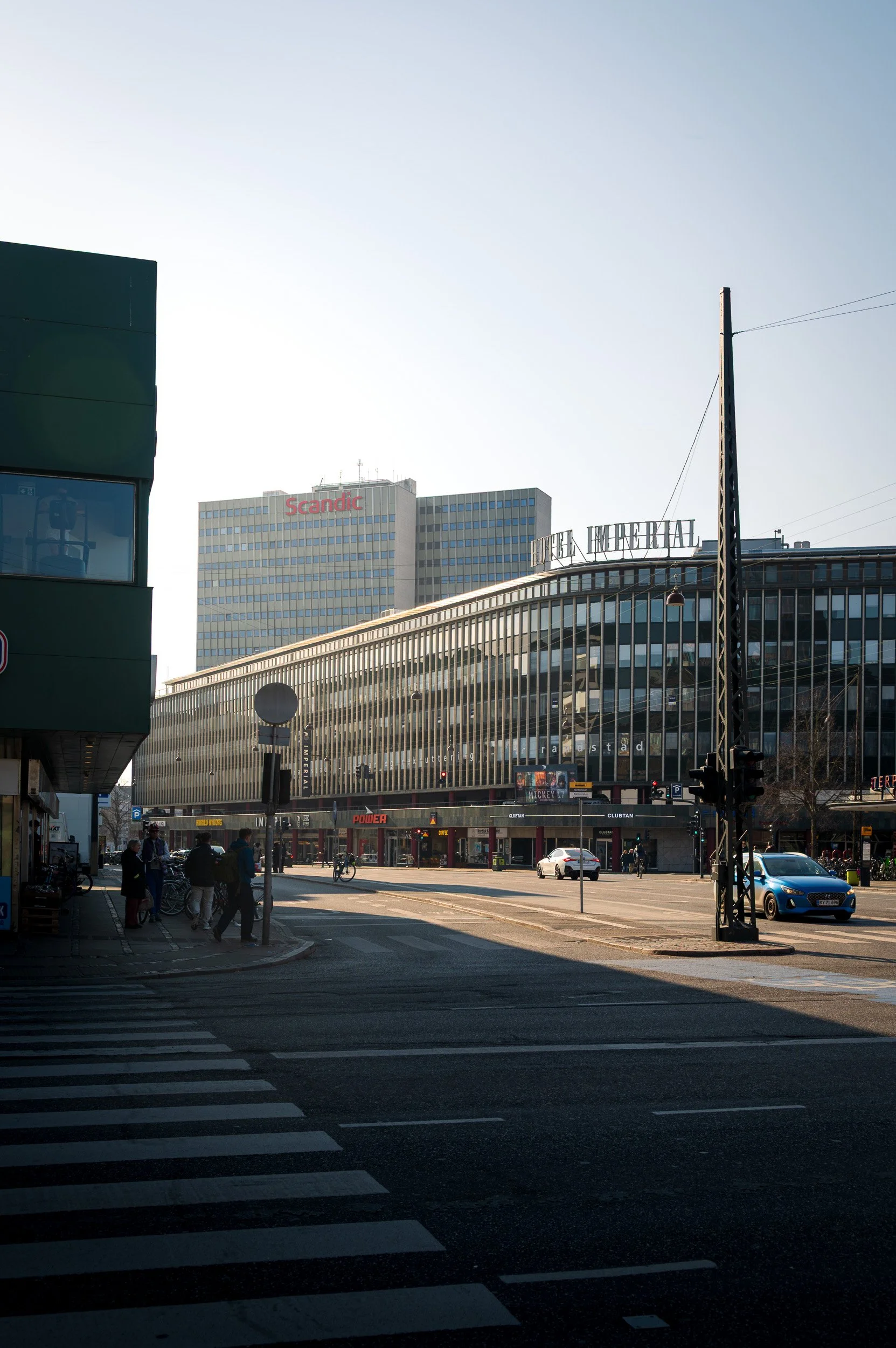 Cityscape photography of the curved Hotel Imperial building in Copenhagen, highlighting long shadows and warm sunlight on the road.