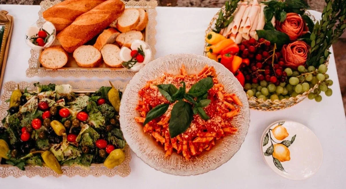 Catering table with bread, Italian salad, penne in red sauce and an antipasto platter