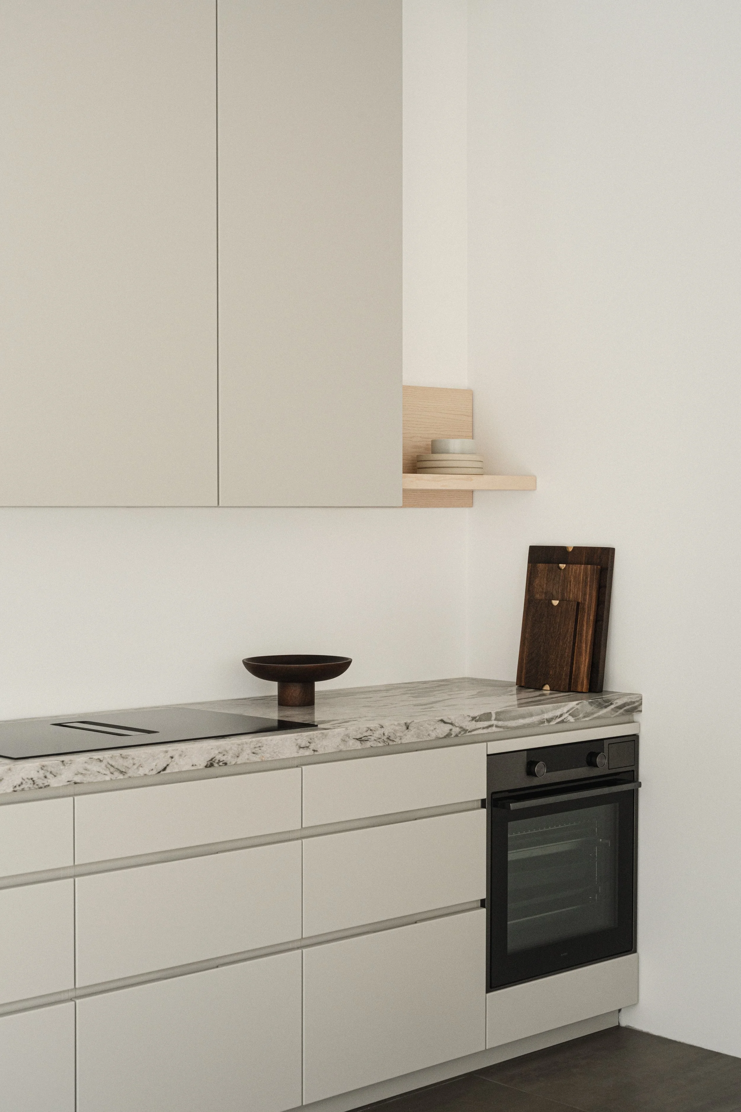 Moderne køkken med hvid cabinetry, grå og hvid marmorbord, kommandoovn, træ knivblikant, mørk trælåg skærebrætter, og en enkelt sort skål på bordet.