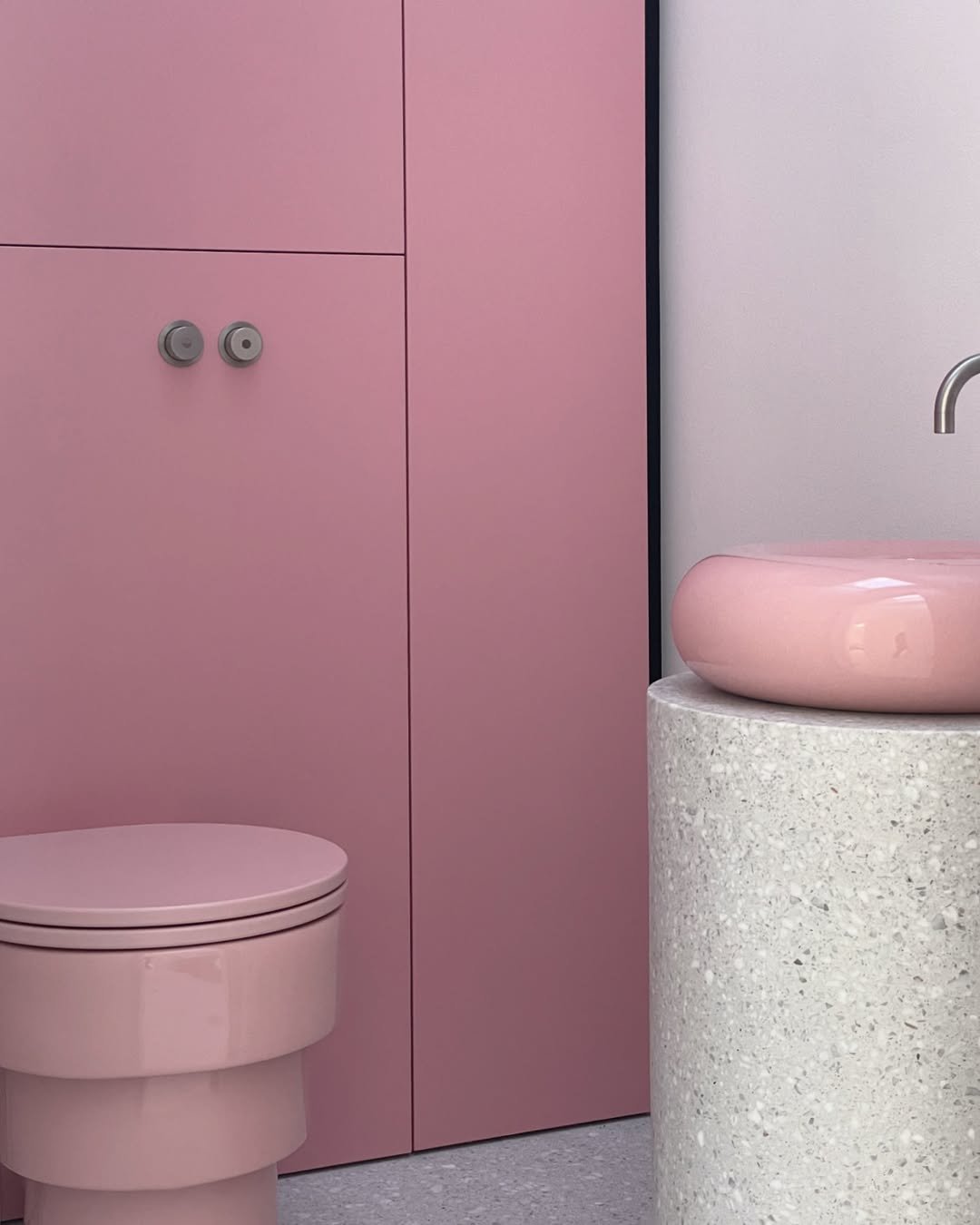 Et badeværelse med lyserøde elementer, herunder toilet, skab, og vask Søjle i terrazzo med pink vask på top.