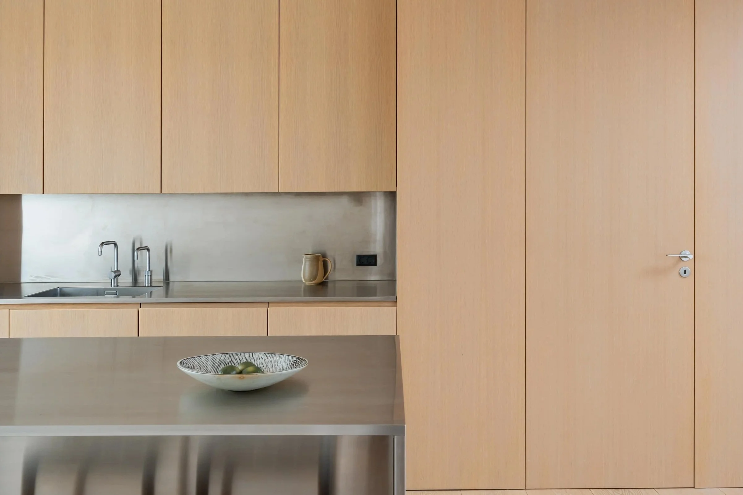 Moderne køkken med træskabe, vask, en kop, en skål med grønne æbler og en låge.