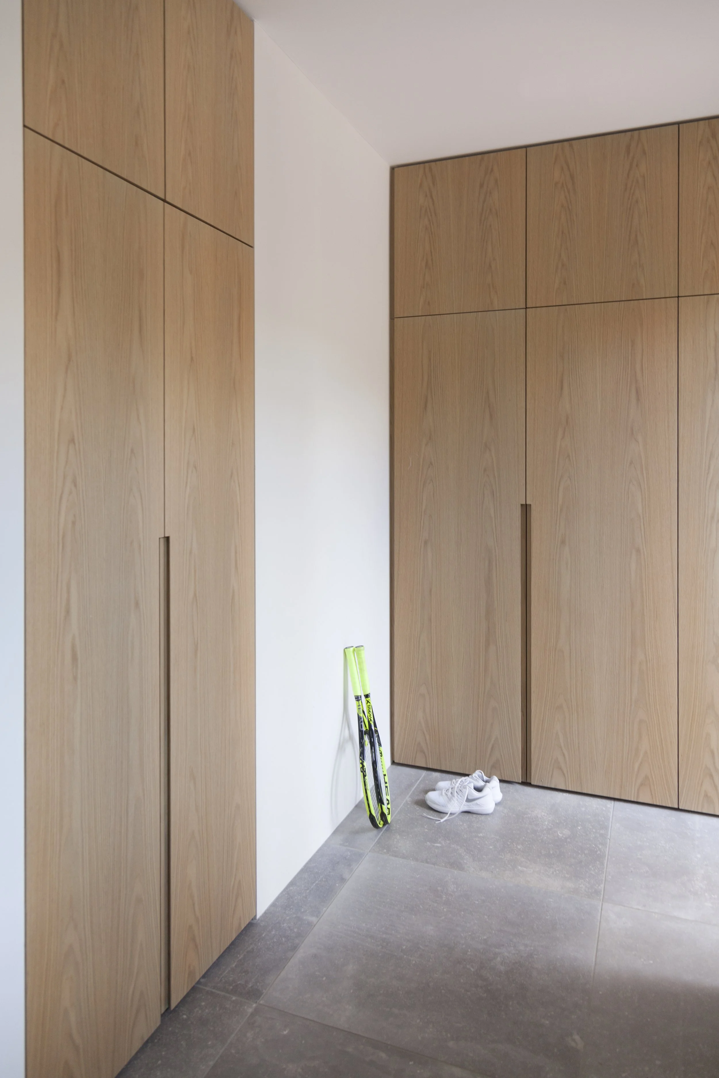 Indgang til et rum med store træskabe, et sæt hvide sportsko og et par skøjter i neongrøn, der er stillet op mod væggen.