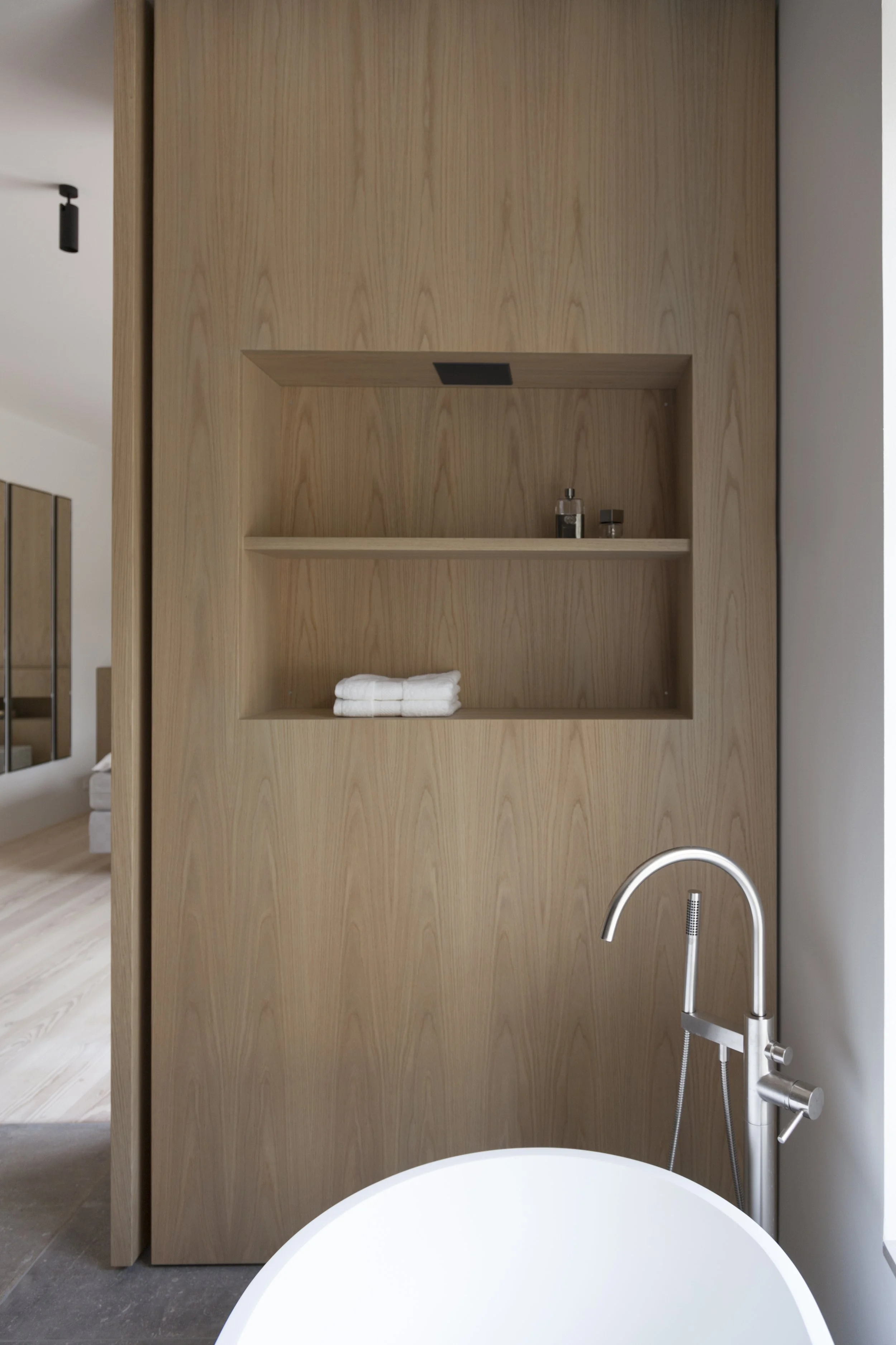 Indvendig badeværelse med trækonstruktion, hylde med håndklæder, toiletartikler og selvstyrende badekar med armatur.