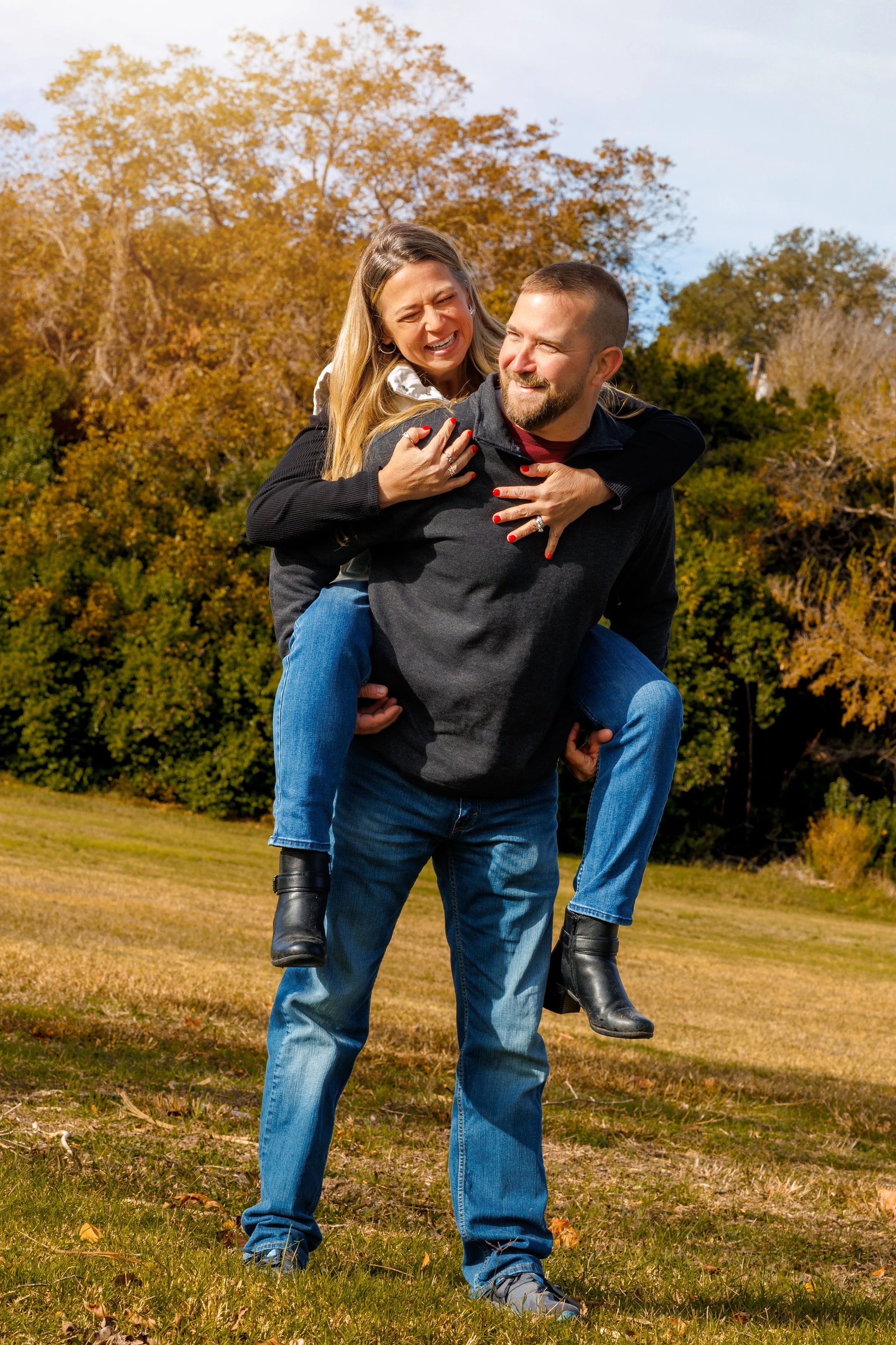 A couple laughing during outdoor engagement-style portrait session in South Mississippi, surrounded by autumn foliage.