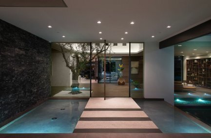 Benedict Canyon Beverly Hills modern luxury home front entrance with walkway over water that leads to floor to ceiling glass walls and indoor living tree