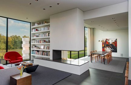 Bright, modern home interior with open plan design that connects a dining room and reading nook library through a peninsula shaped fireplace