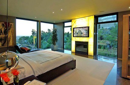 Modern luxury bedroom with backlit onyx fireplace and glass walls at our 9288 Sierra Mar house in the Hollywood Hills