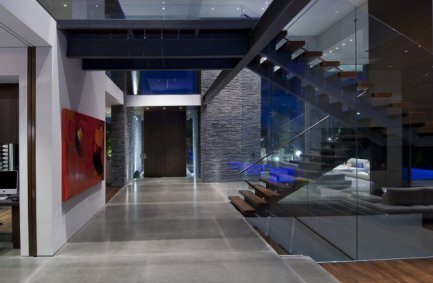 Front door and open volume interior with glass encased switchback staircase at out Summit House in Beverly Hills