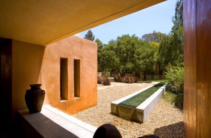 Minimalist landscape design features a rectangular stretch of water alongside earth toned exterior walls