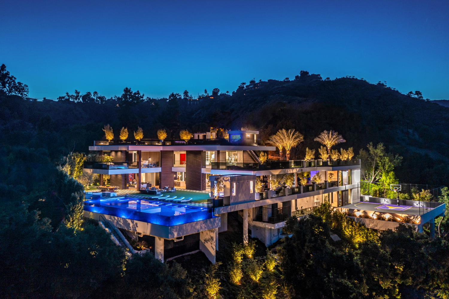 Bundy Drive luxury modern mansion with terraced indoor outdoor design and infinity pool, lit up at night