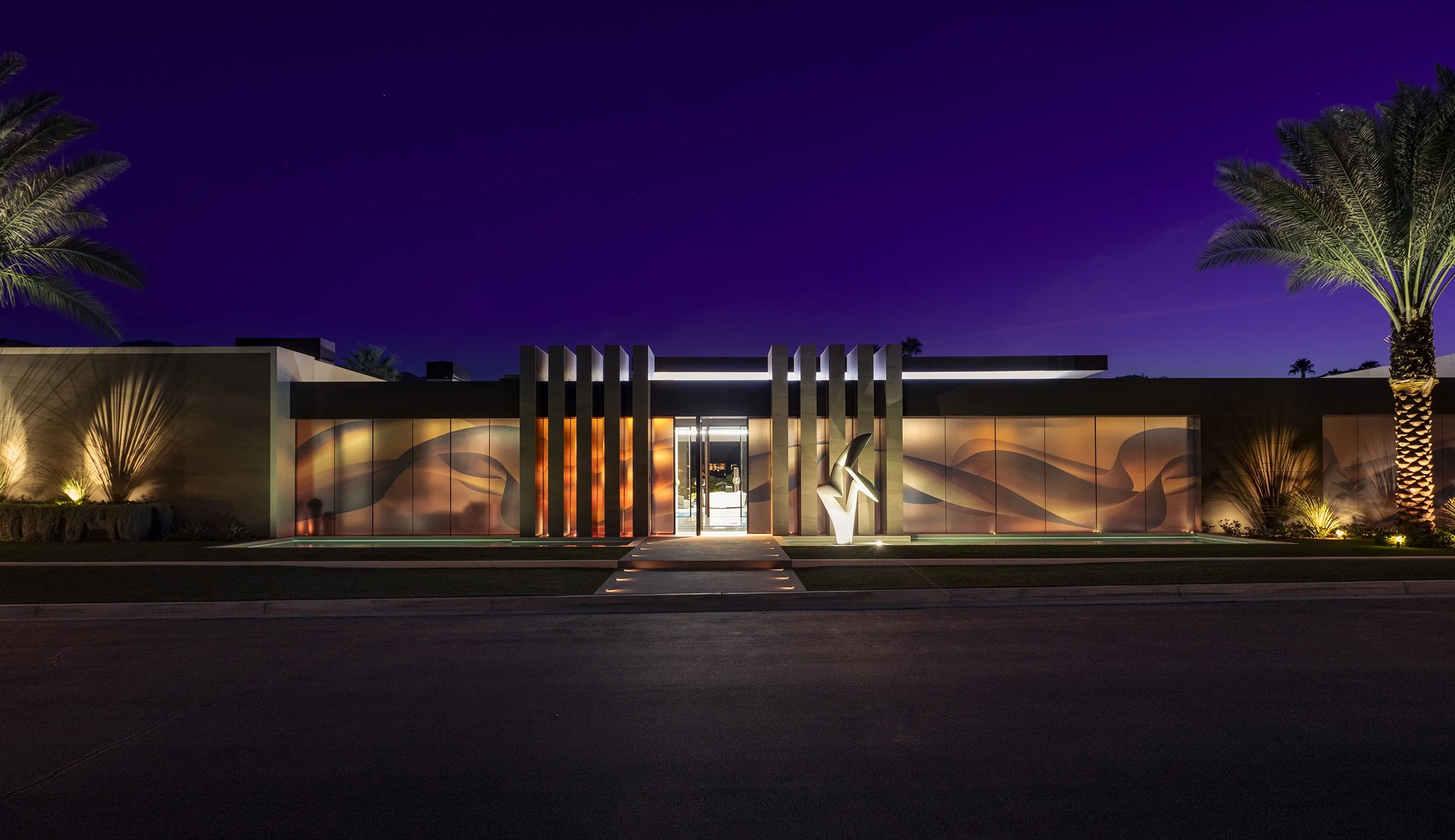 Serenity modern desert mansion in Indian Wells, California at night with illuminated entryway, bold architectural lines, and glass wall mural