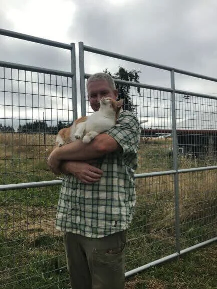Photo of Brad holding Sherbert, an orange and white cat at April Joy Farm.