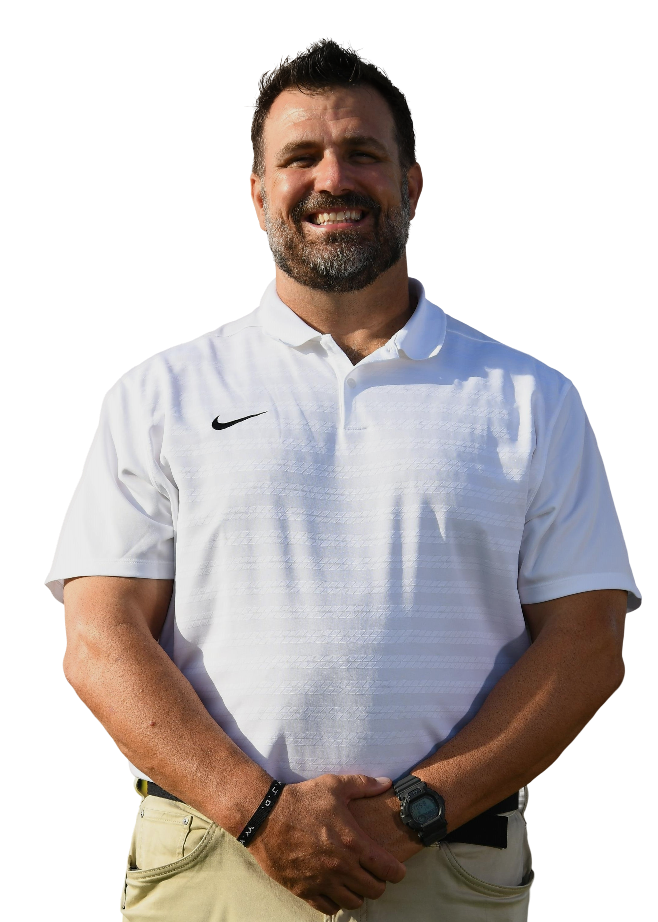 A man with a beard and short hair wearing a white shirt and khaki pants, standing outdoors with his hands clasped. He is smiling and looking at the camera.
