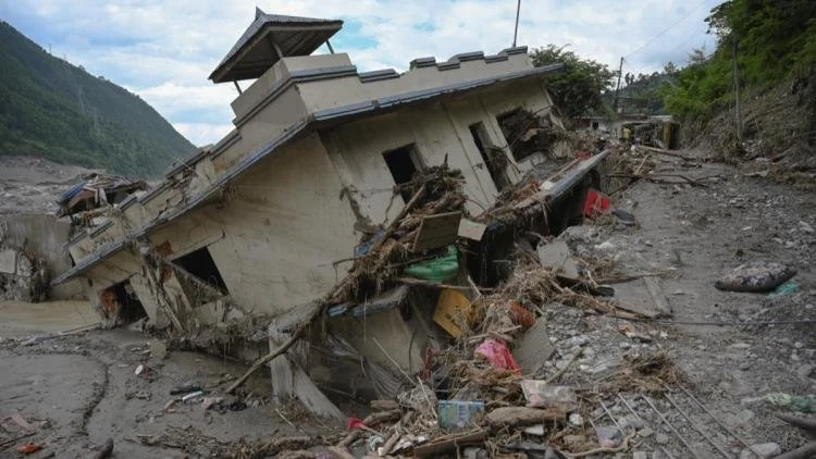 Népal. Une maison effondrée et dévastée après une catastrophe naturelle, avec des débris et un terrain accidenté autour.