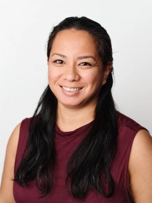 A woman with long black hair, smiling, wearing a sleeveless maroon top, against a plain white background.