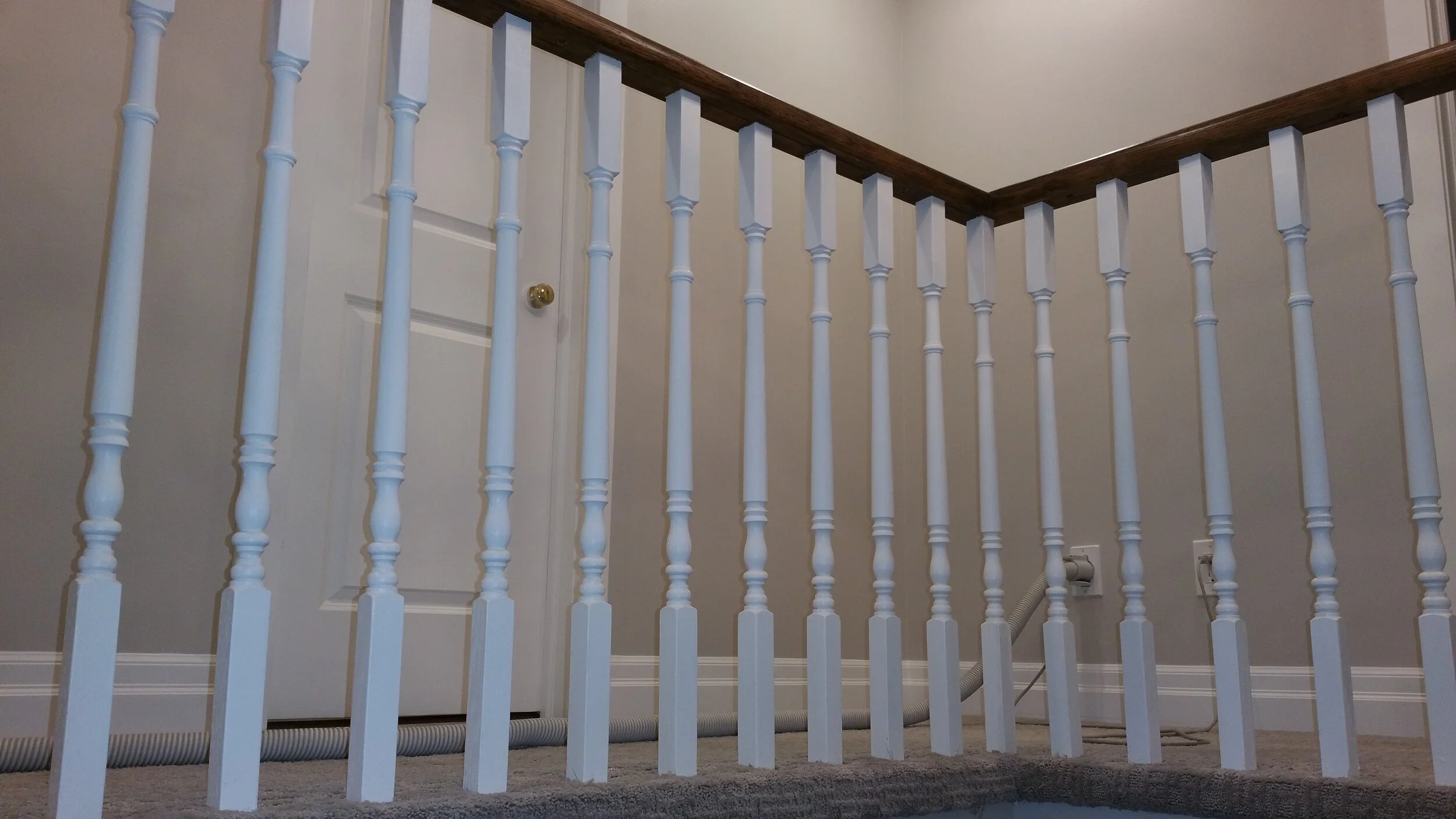 View of a staircase railing with white spindles and a brown wooden handrail Interior House Painting. Heather Feather Painting and Design. Toronto. Spraying. Stair Refinishing.