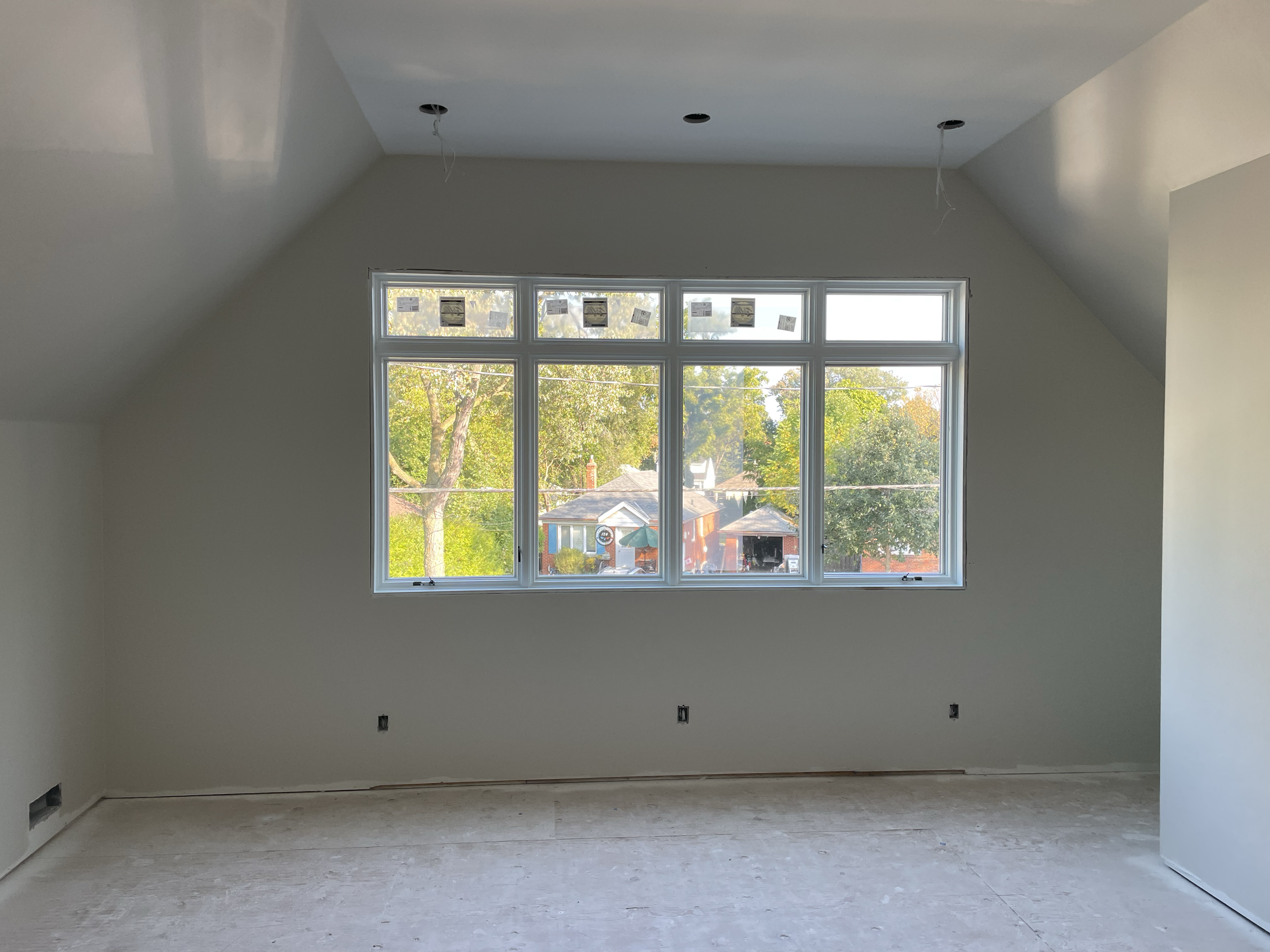 Empty room under construction with large window showing trees outside and ceiling with recessed lighting fixtures being installed.
Interior House Painting. Heather Feather Painting and Design. Toronto. Spraying.